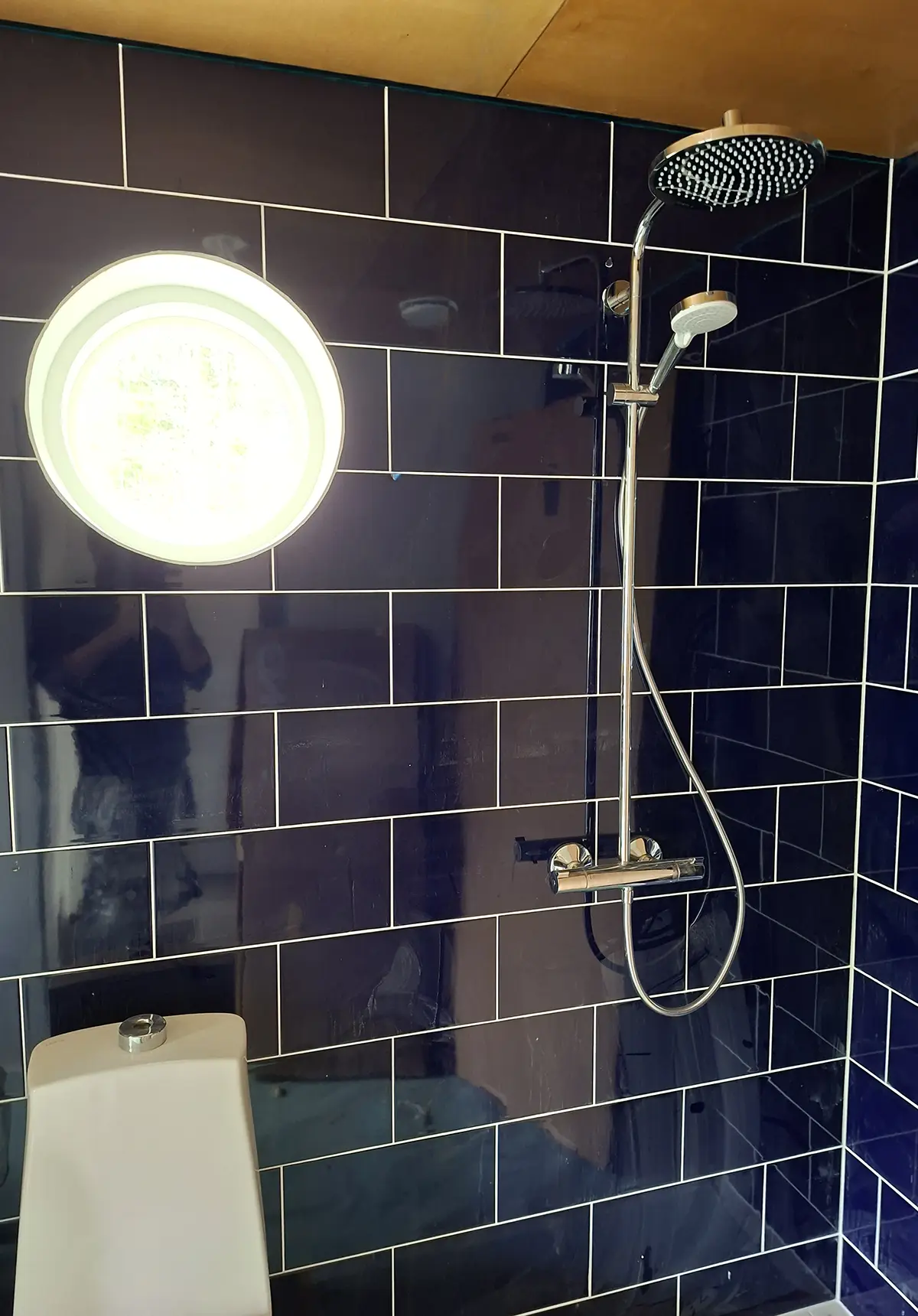 Kylpyhuoneremontti. Tummat kiiltävät kaakelit, tiililadonta ja vaaleat saumat.