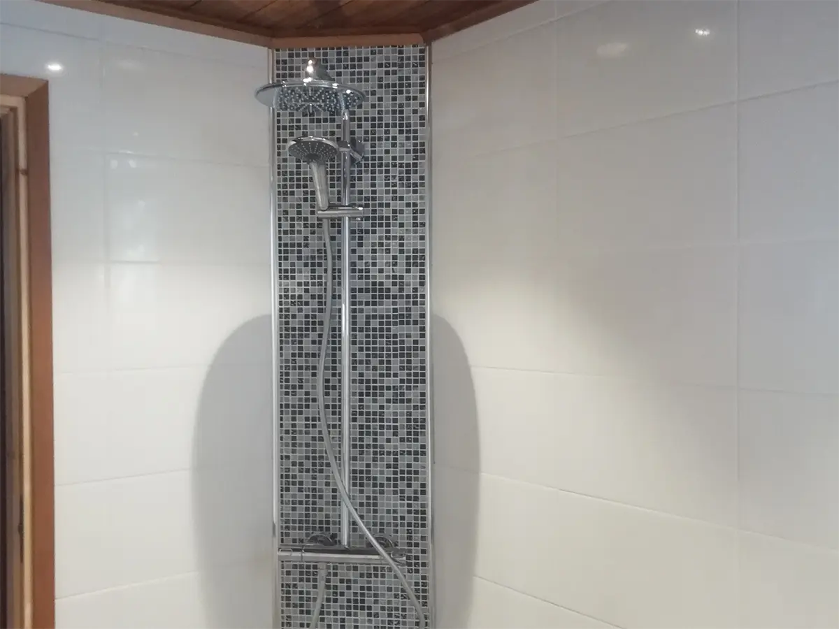 Remontoitu suihkutila, jossa valkoiset kaakeliseinät ja mosaiikkilaatoilla rajattu suihku.