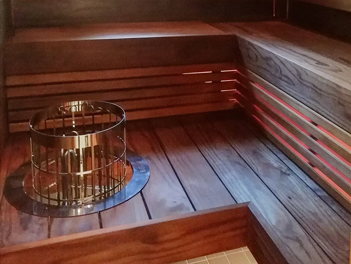 Tummasävyinen sauna, jossa puupintaiset lauteet ja kiuas vielä ilman kiuaskiviä.