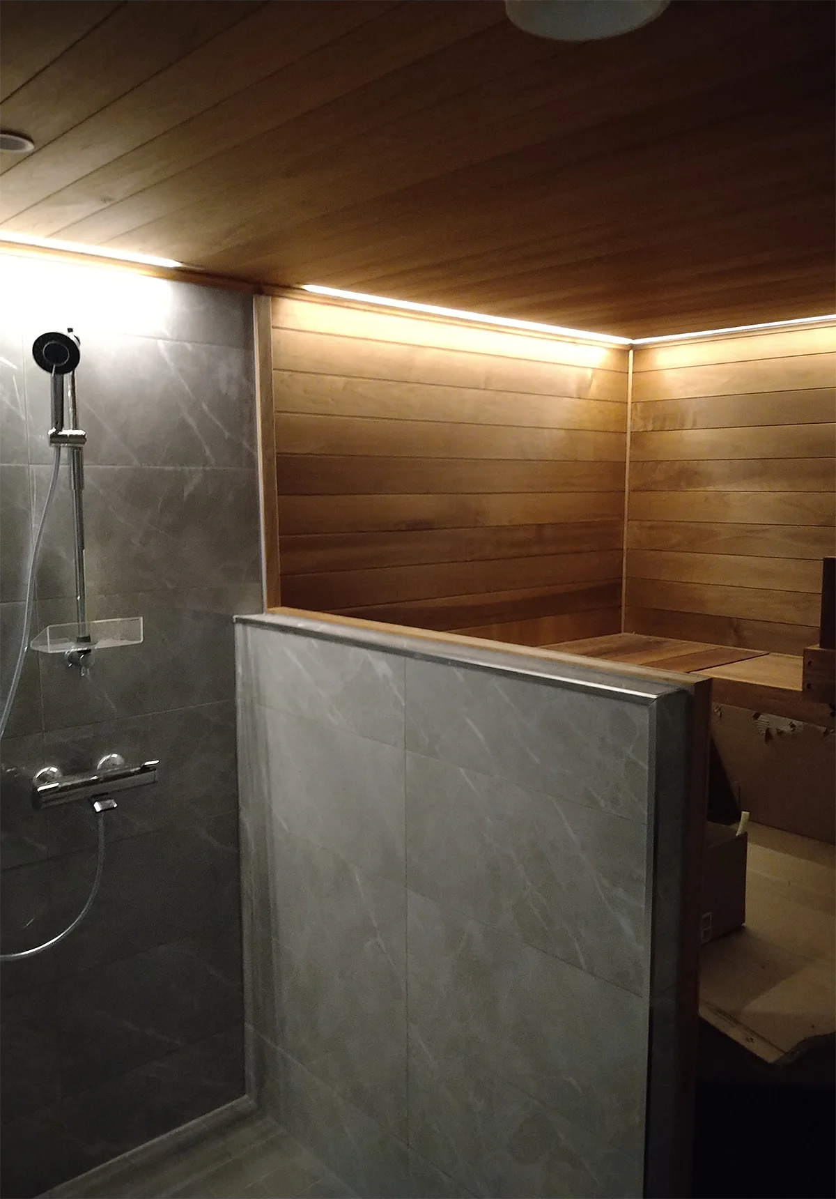 Moderni, tunnelmallinen sauna puupaneloituna, harmailla laattaseinillä ja pehmeällä LED-valaistuksella.